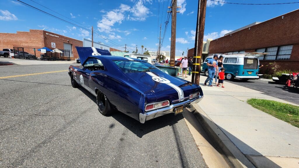 Classic blue muscle car with white racing stripes parked on street.