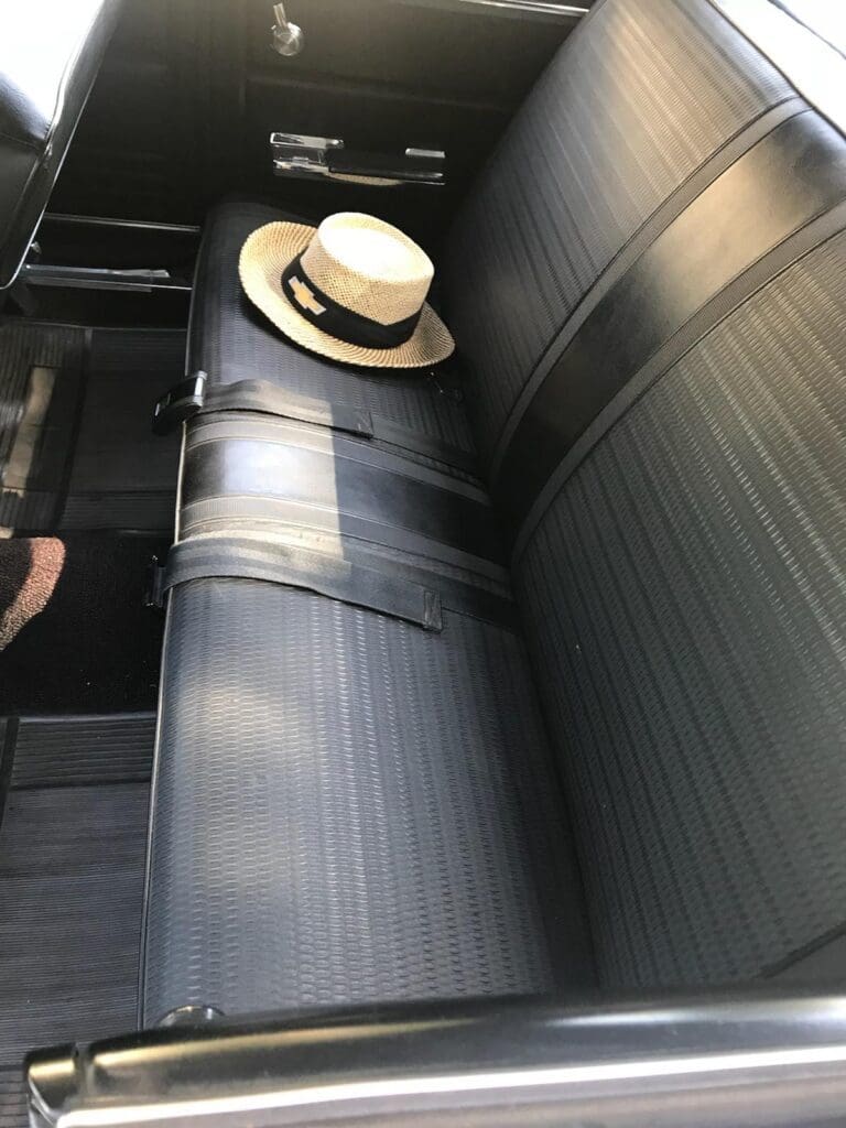 A straw hat resting on the backseat of a car with black upholstery.