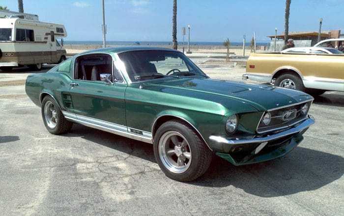 Classic green Ford Mustang parked near the beach on a sunny day.