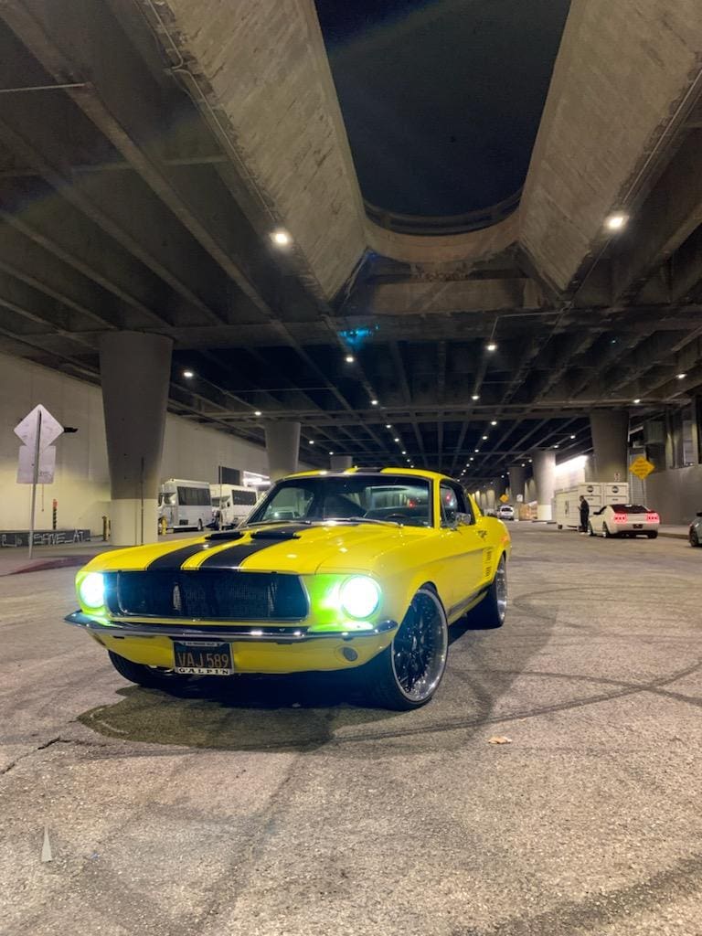Yellow classic car with black stripes parked under a bridge at night.