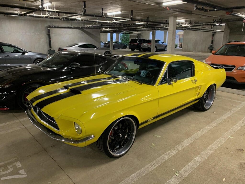 Yellow classic Ford Mustang with black racing stripes in a parking garage.