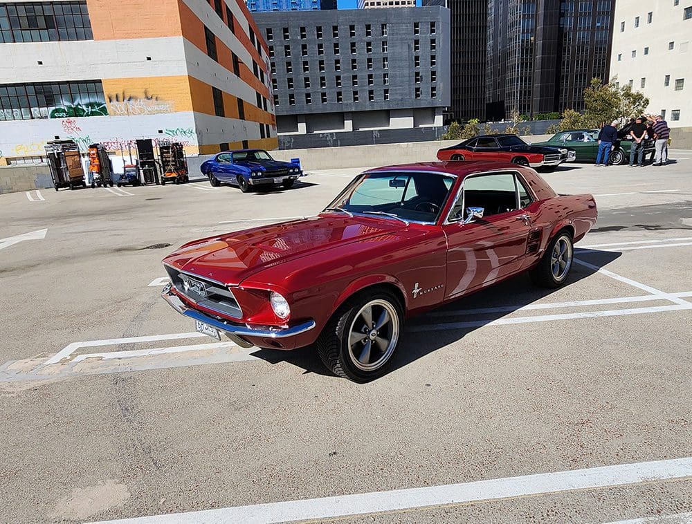 Classic red Mustang parked in an urban lot under clear skies.