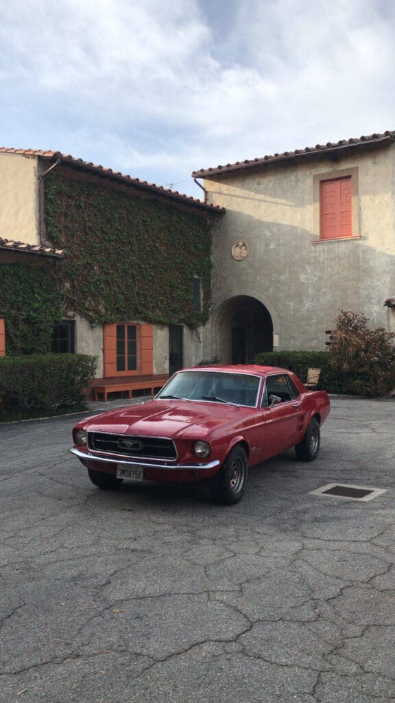 Classic red muscle car parked in front of a rustic house.