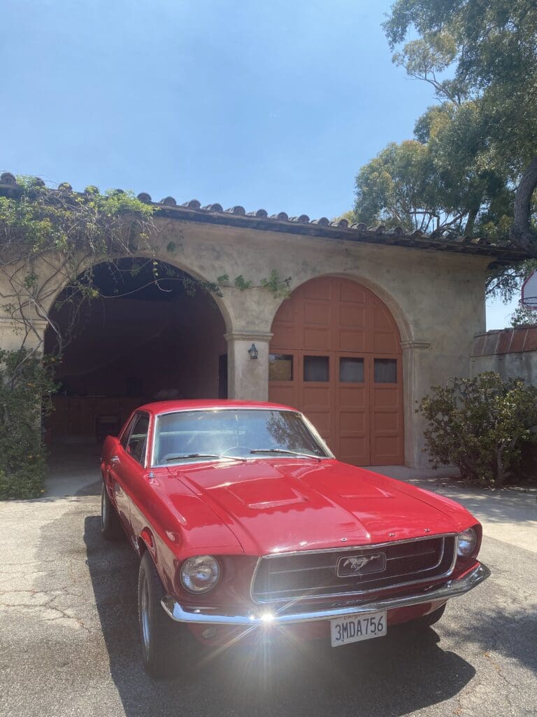 Red vintage car parked in front of a rustic building with arched doorways.