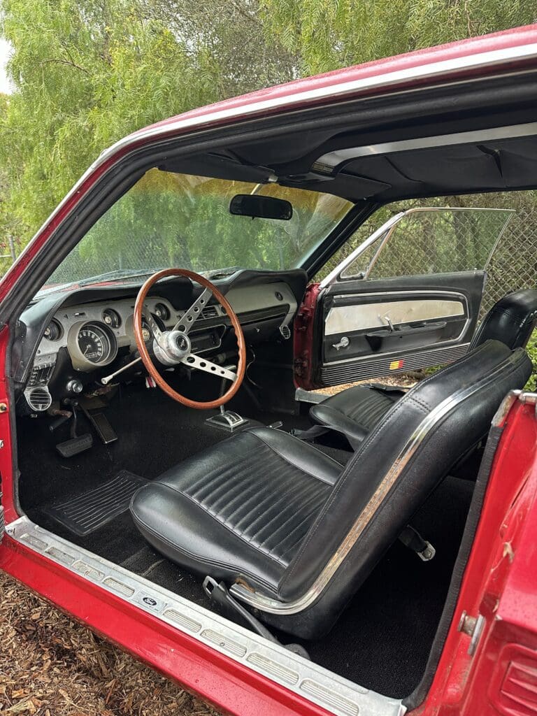 Interior of a classic car with black leather seats and wooden steering wheel.
