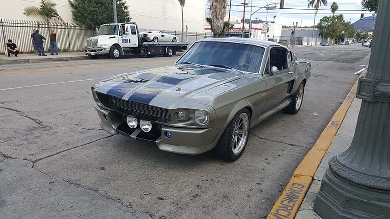 Classic silver Ford Mustang parked on the street with racing stripes.