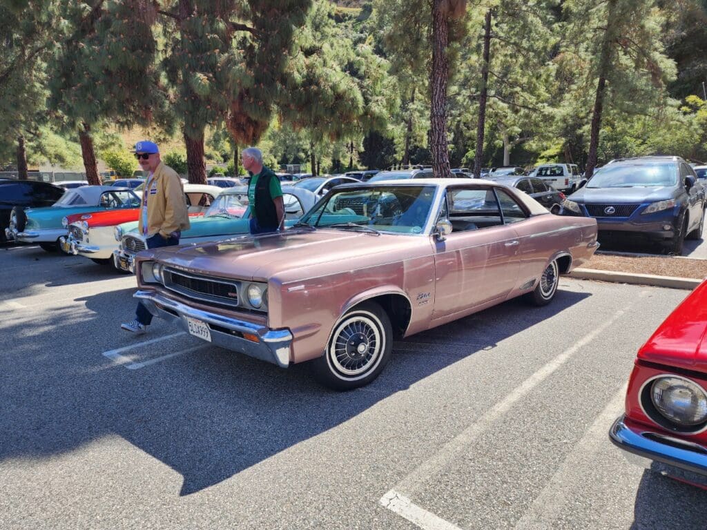Vintage pink Cadillac parked at an outdoor car show under sunny skies.