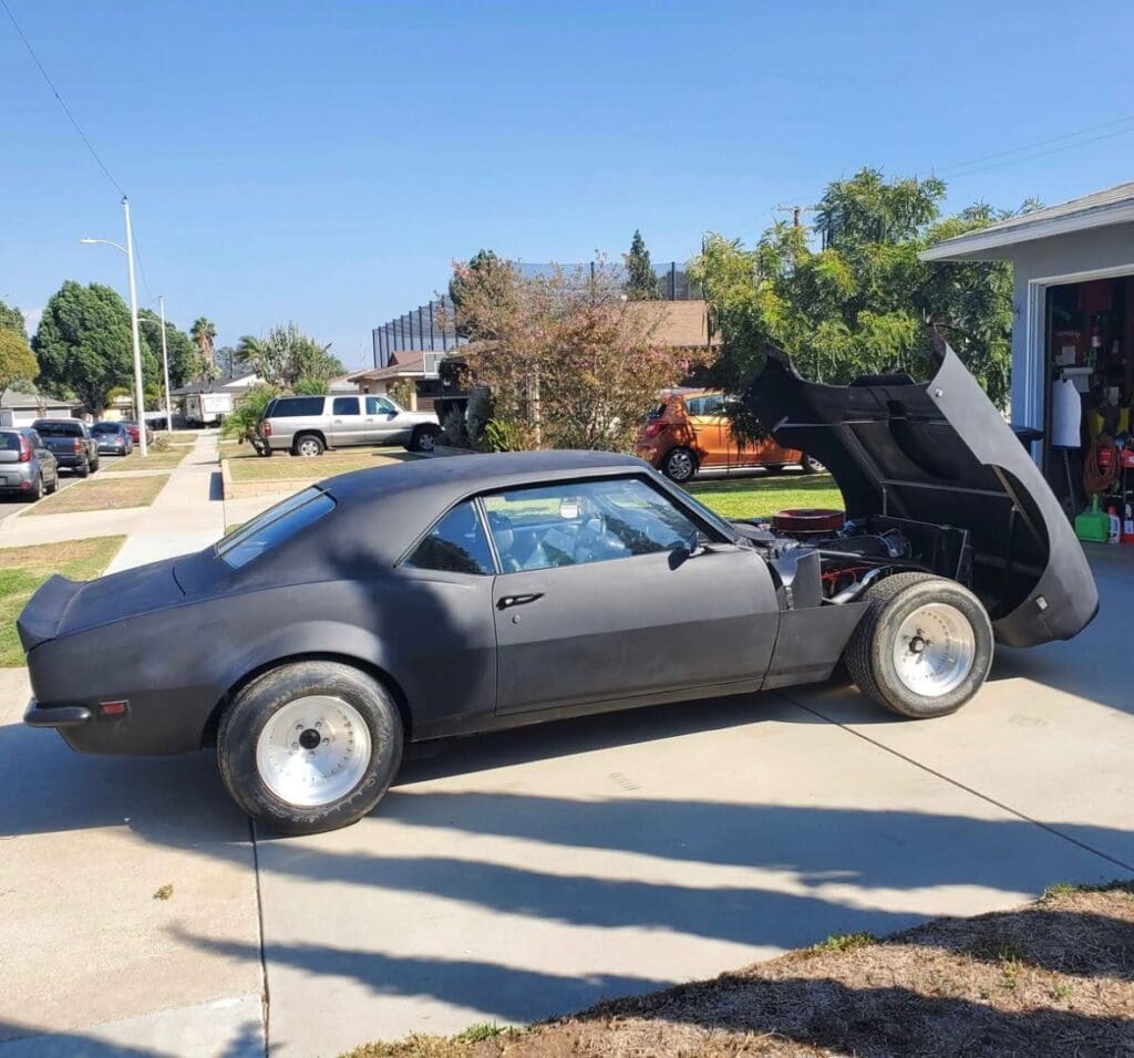Classic black muscle car parked with its hood open on a sunny day.