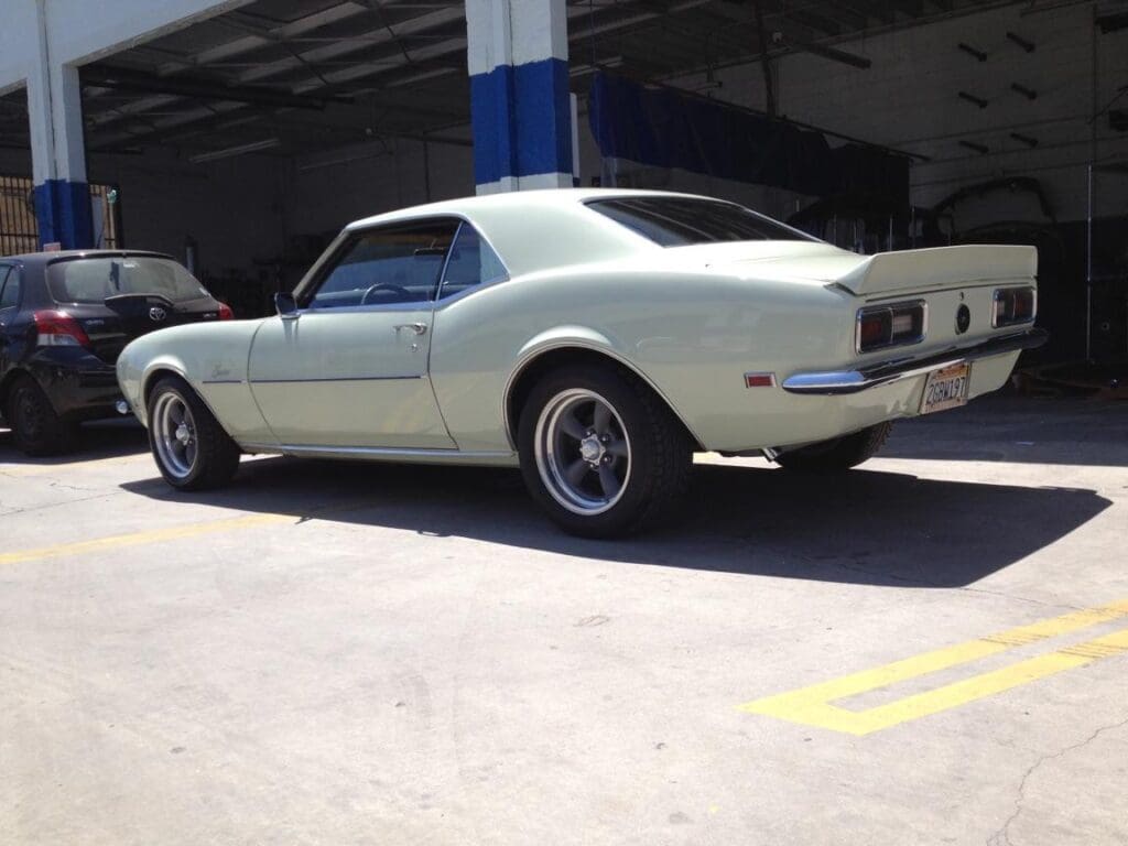 Classic light green Chevrolet Camaro parked outdoors near a garage.