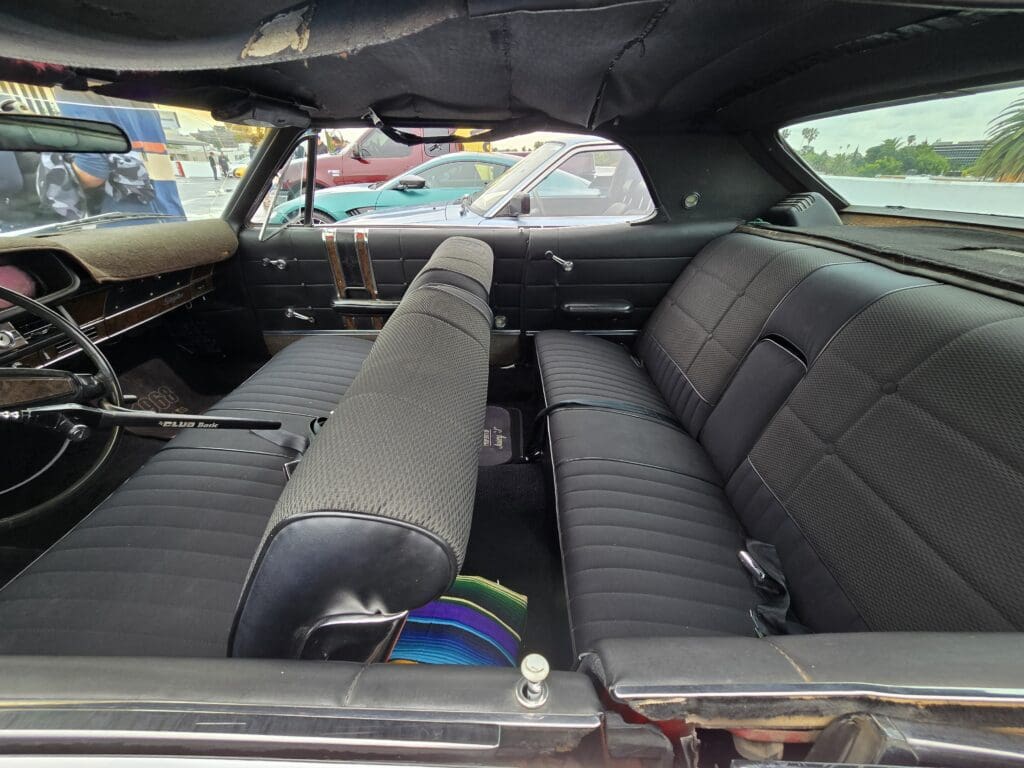 Interior view of a vintage car with black leather seats and a rear seat folded forward.