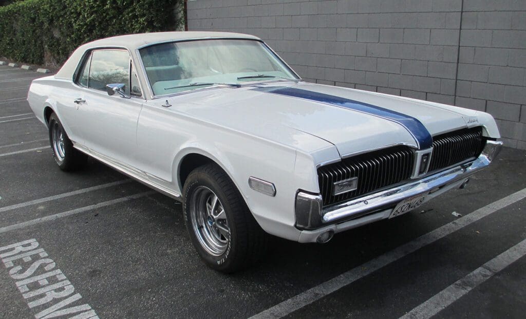 Classic white Mercury Cougar with blue racing stripes parked outdoors.