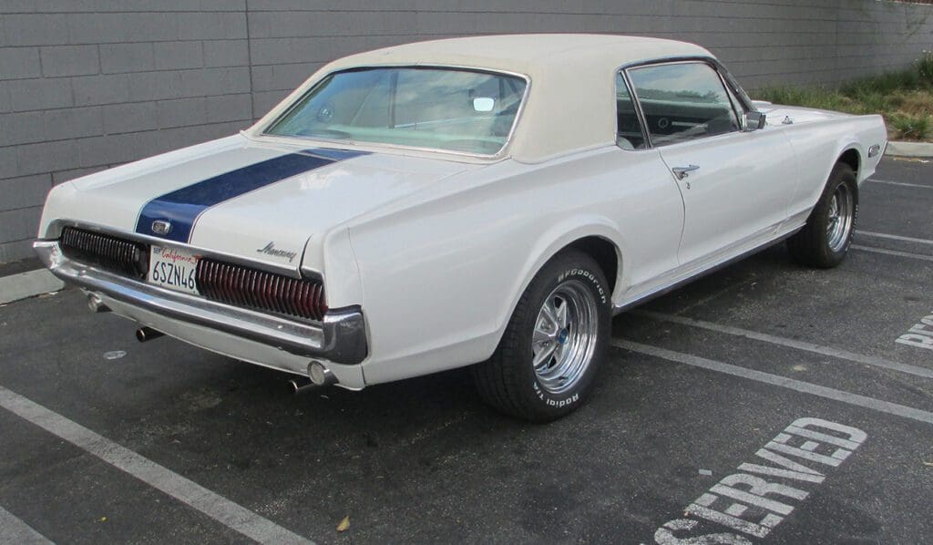 Classic white Mercury Cougar with a blue racing stripe parked outdoors.