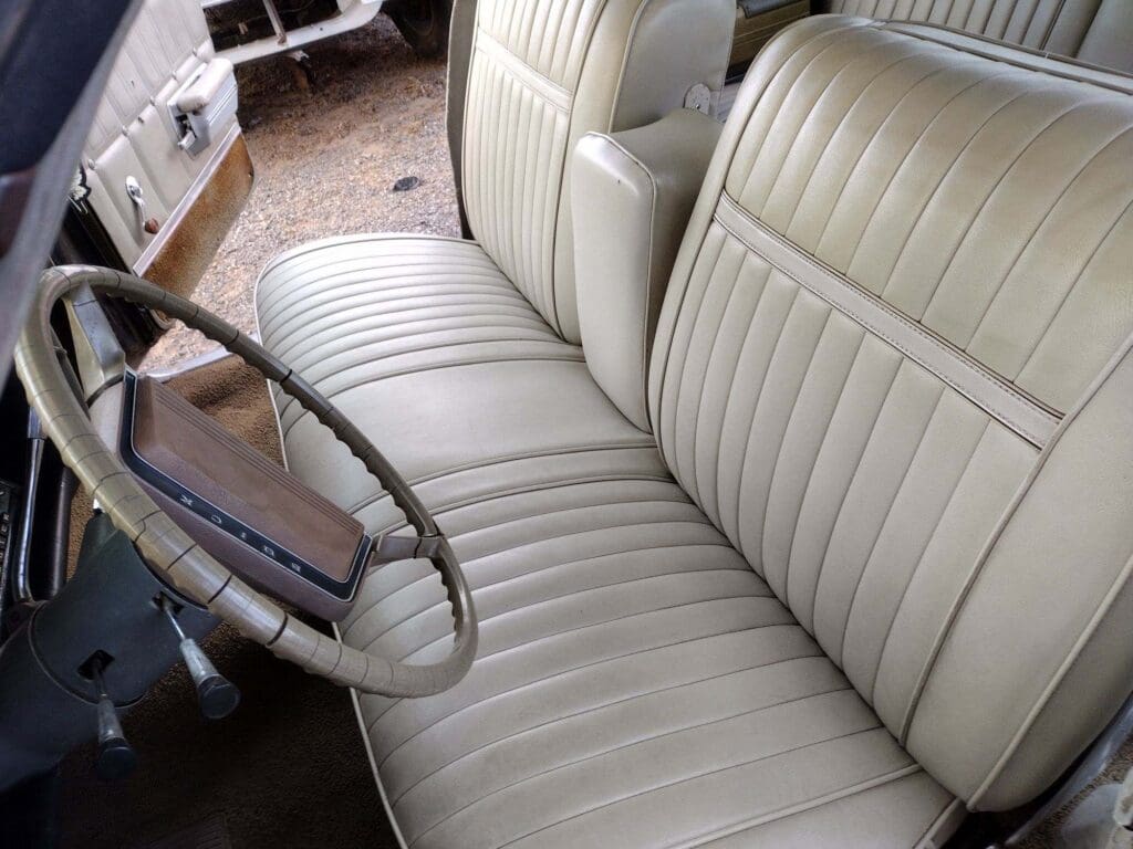 Classic car interior with cream leather bench seat and vintage steering wheel.