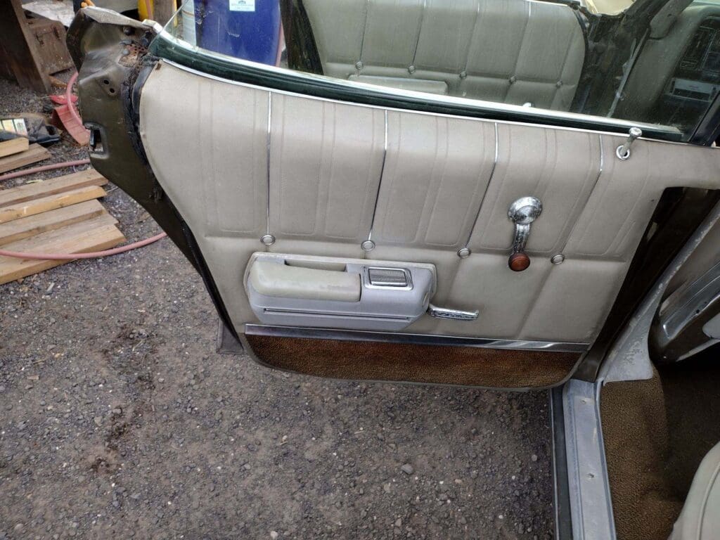 Interior door panel of a vintage car with beige upholstery and wood trim.