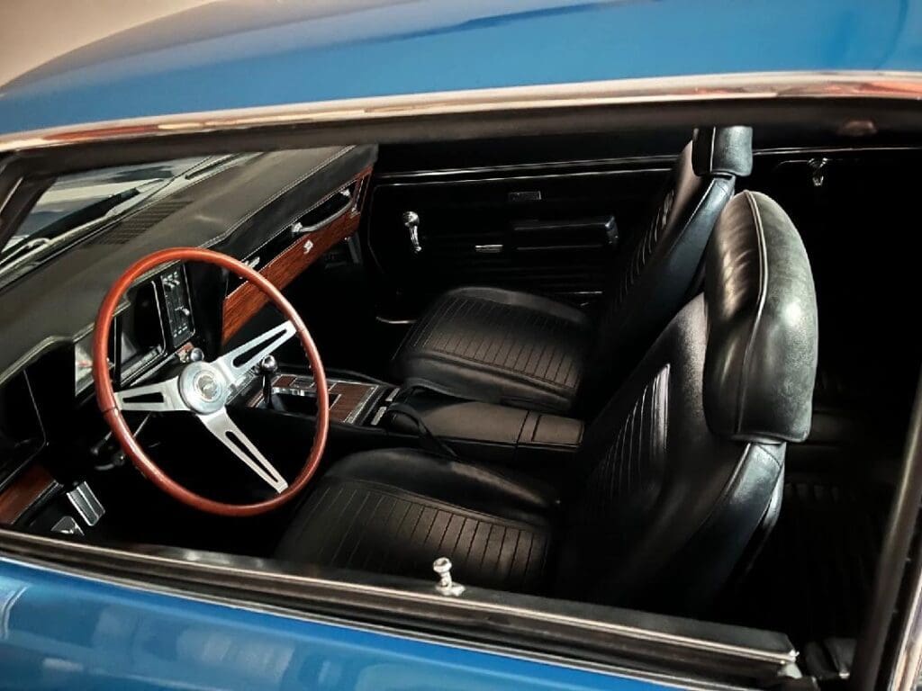 Interior of a classic car with black leather seats and a wooden steering wheel.
