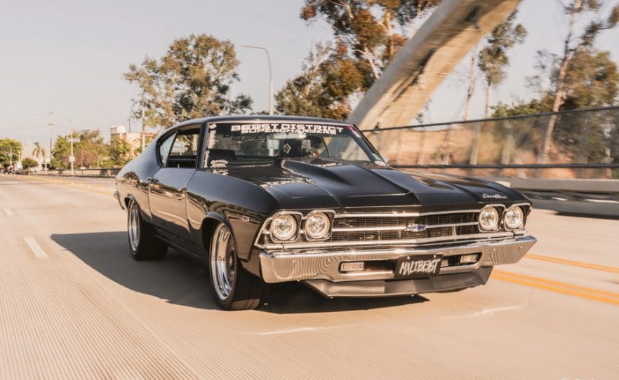 Classic black muscle car driving on a sunny road.
