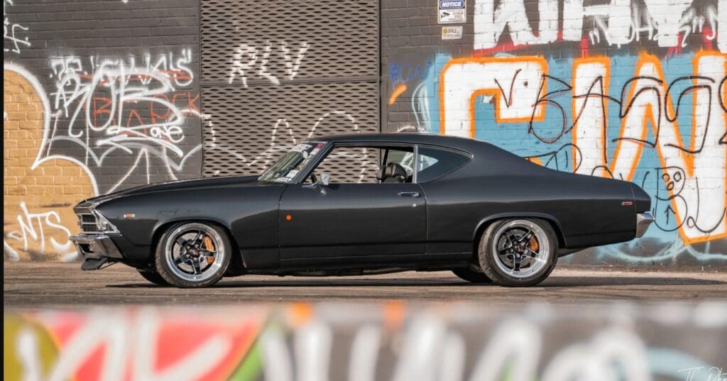 A sleek black sports car parked in front of a graffiti wall.