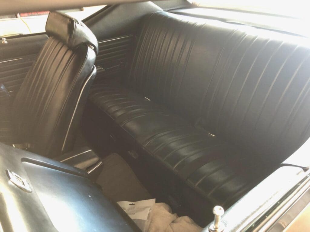 Interior view of a classic car's black leather backseat.