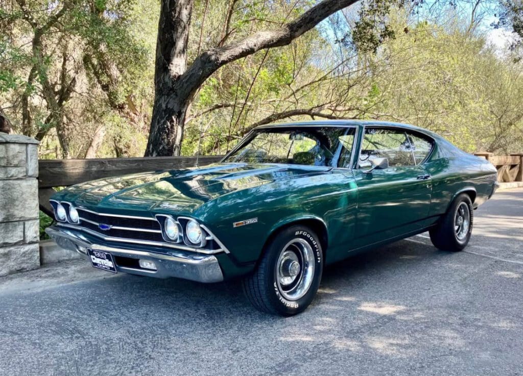 Classic green 1960s muscle car parked under trees.