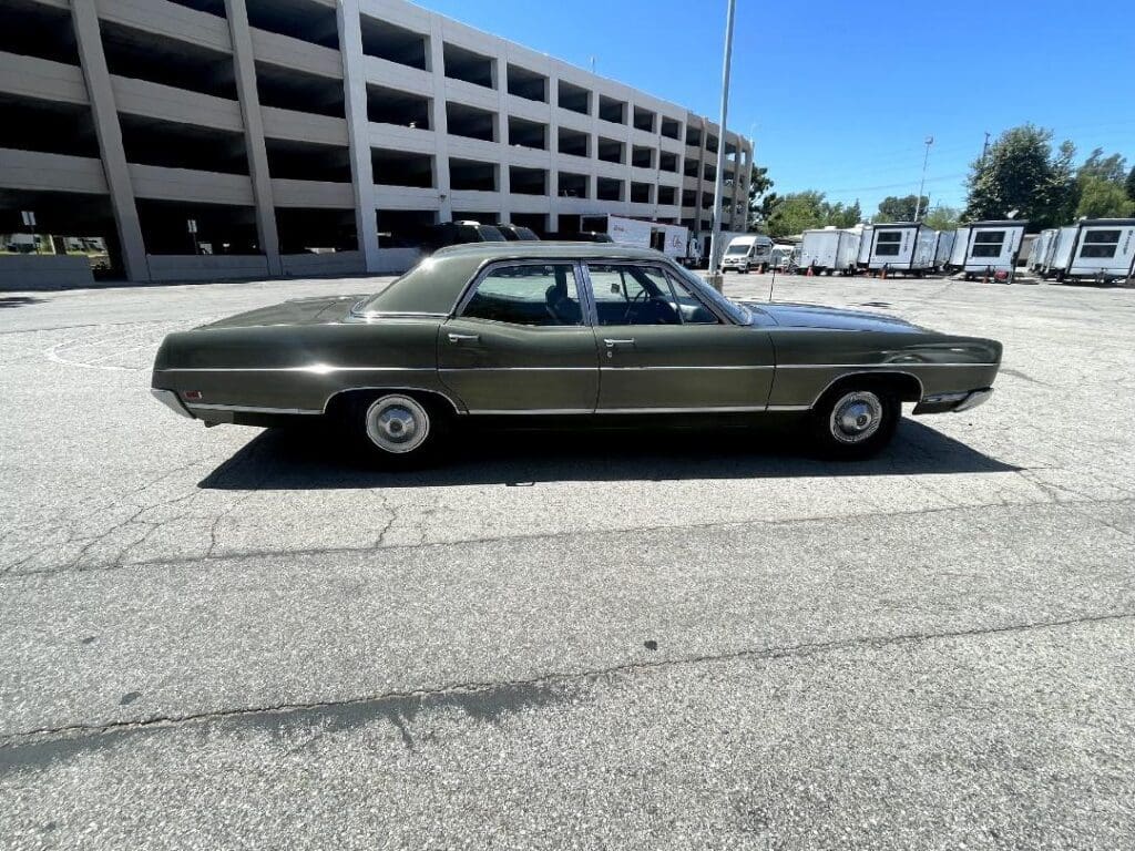 Classic dark green vintage car parked near a multi-level parking garage.