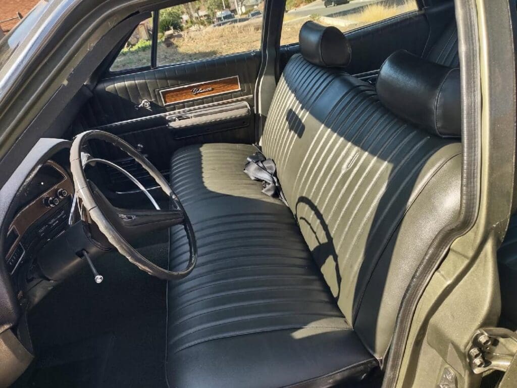 Vintage car interior with black leather bench seat and classic steering wheel.