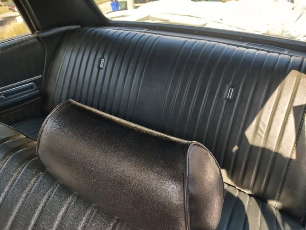 Vintage black leather car backseat with a cushioned headrest.