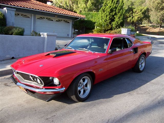 Classic red 1969 Ford Mustang parked on a sunny street.
