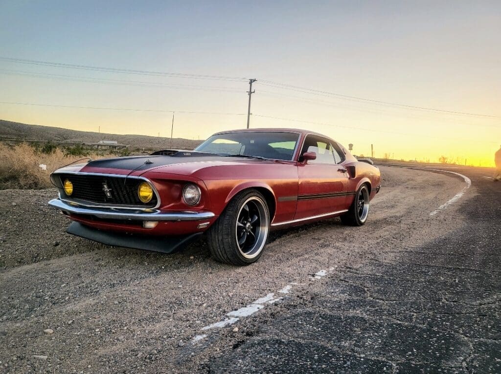 Classic red Ford Mustang parked on an empty road at sunset.