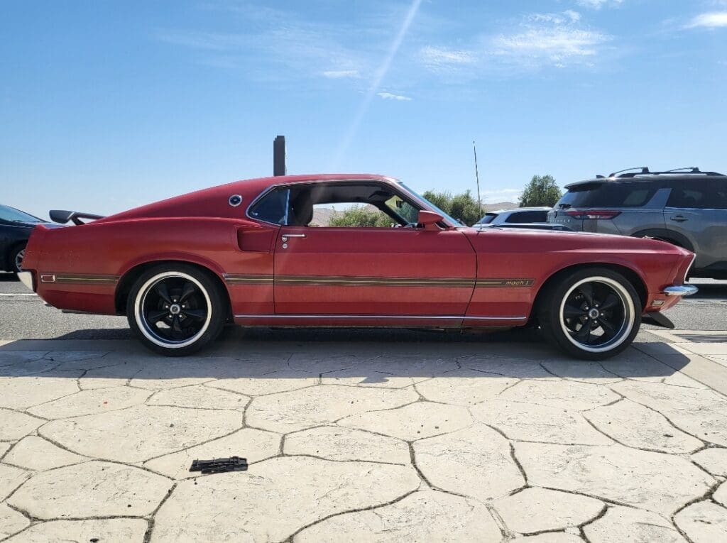 Red classic muscle car parked on cracked pavement under clear sky.