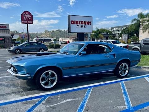 A blue classic muscle car parked in a handicapped spot near a tire shop.