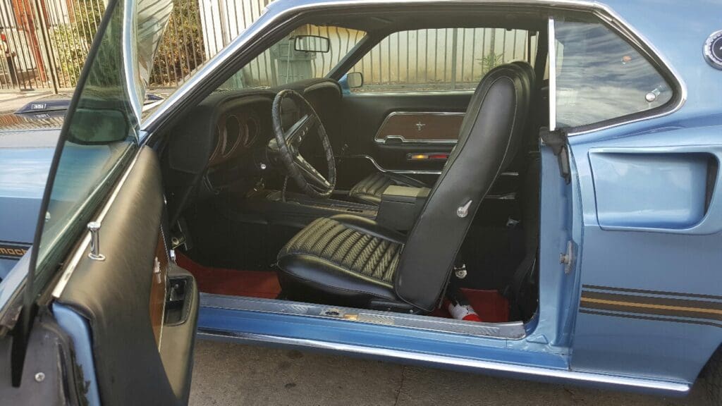 Interior of a classic blue car with black bucket seats and a vintage dashboard.