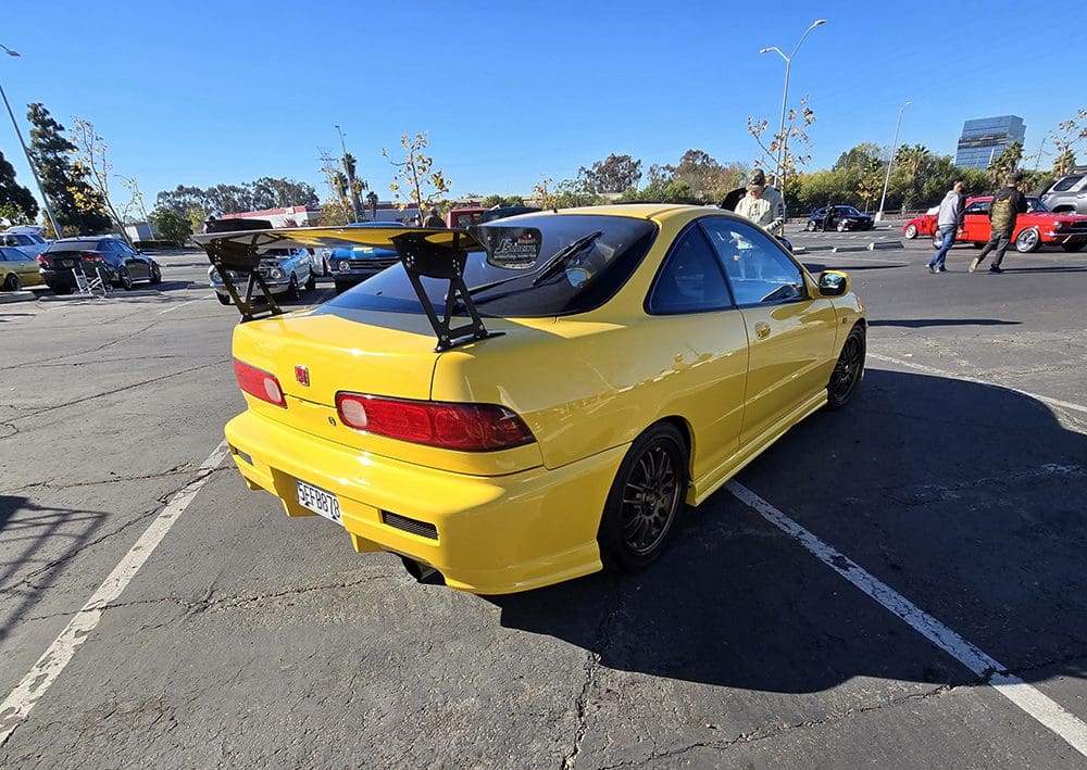 Yellow modified sports car parked in a lot under clear skies.