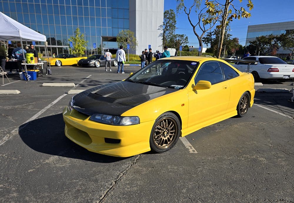Yellow sports car with black hood parked outdoors on a sunny day.