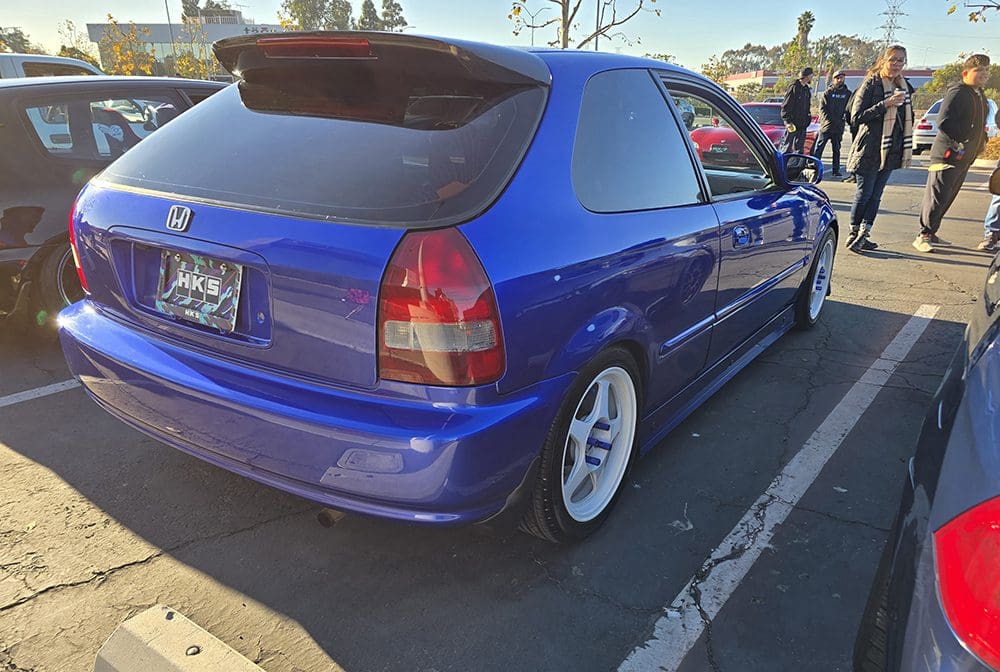 Blue hatchback car parked in a lot with white wheels.