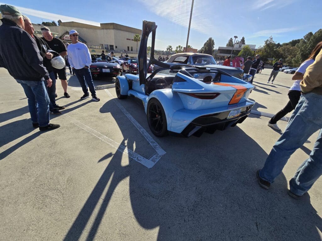 A blue sports car displayed at an outdoor car show with spectators.