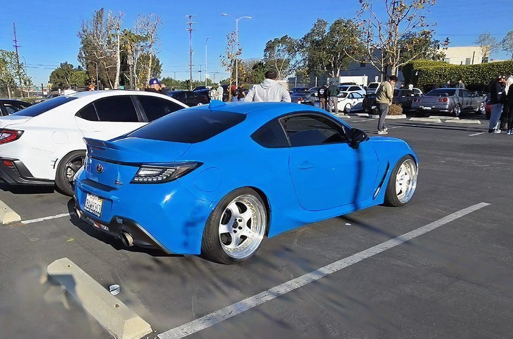 A blue sports car with modified wheels parked in a lot.