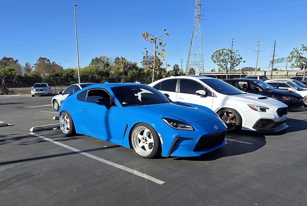 A bright blue sports car parked in a sunny lot beside other vehicles.