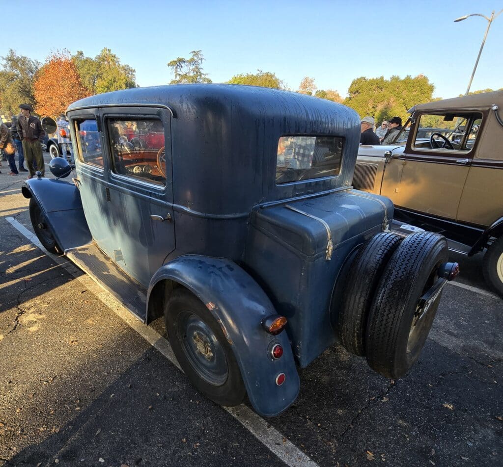 Vintage blue car parked outdoors with autumn trees in background.