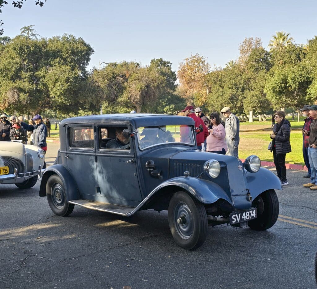 Vintage blue car parked at an outdoor gathering with people around.