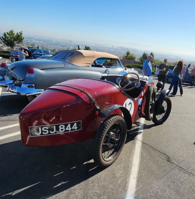 Vintage red racing car at a classic car show by the sea.