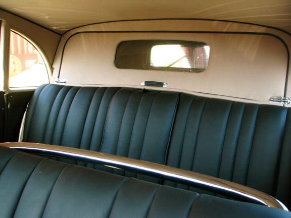 Interior of a vintage car with black leather seats and a rearview mirror.