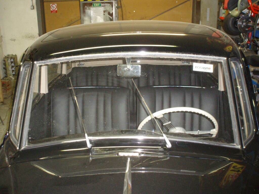 Vintage car interior with a white steering wheel and split windshield.