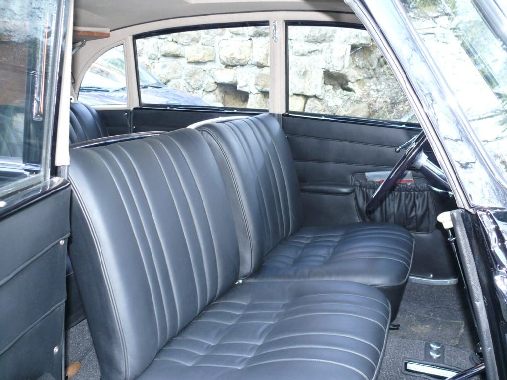 Vintage car interior with black leather bench seat and steering wheel.
