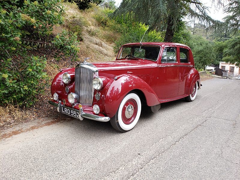 A classic red vintage car parked on a roadside with whitewall tires.