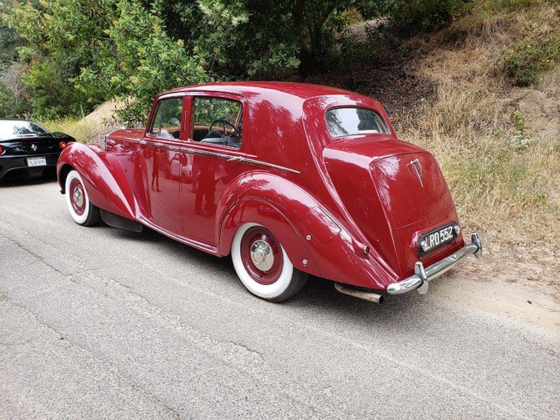 A classic red vintage car parked on a roadside with whitewall tires.