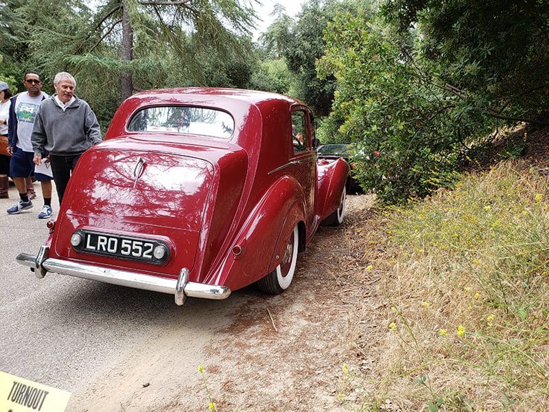 A vintage red car parked on a dirt path surrounded by greenery.