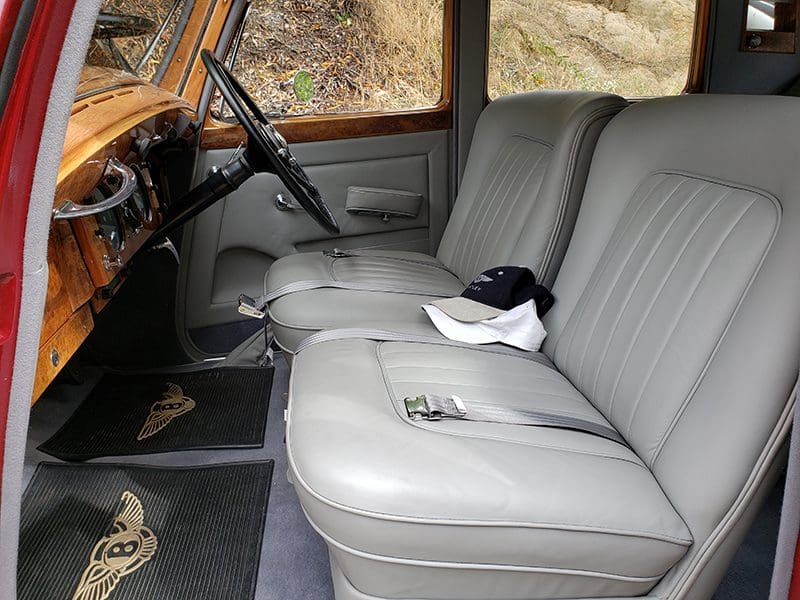 Interior of a classic car with gray leather seats and a white cap on the passenger seat.