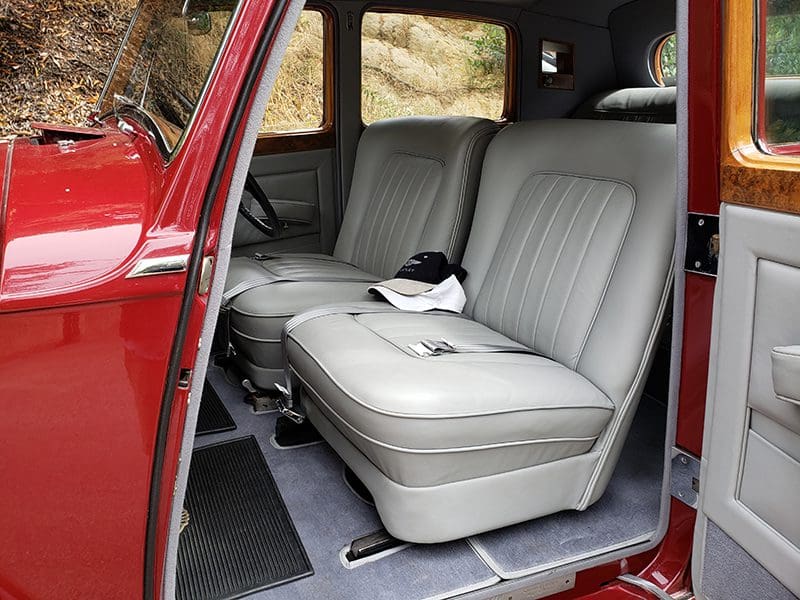 Interior view of a vintage vehicle with gray leather seats and a red door.
