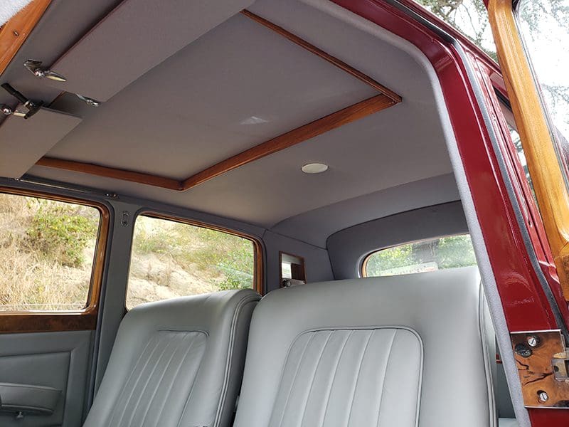 Interior view of a vehicle with white leather seats and a wooden ceiling panel.