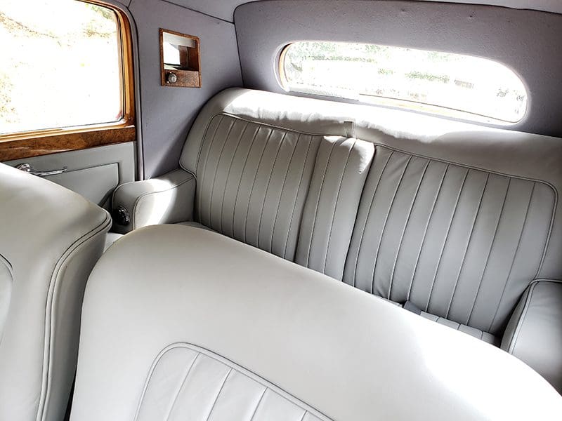 Interior of a classic car with light-colored leather seats and wood paneling.
